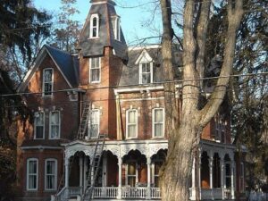 tree in the foreground and slate roof sartore residence in the back with ladders against the brick