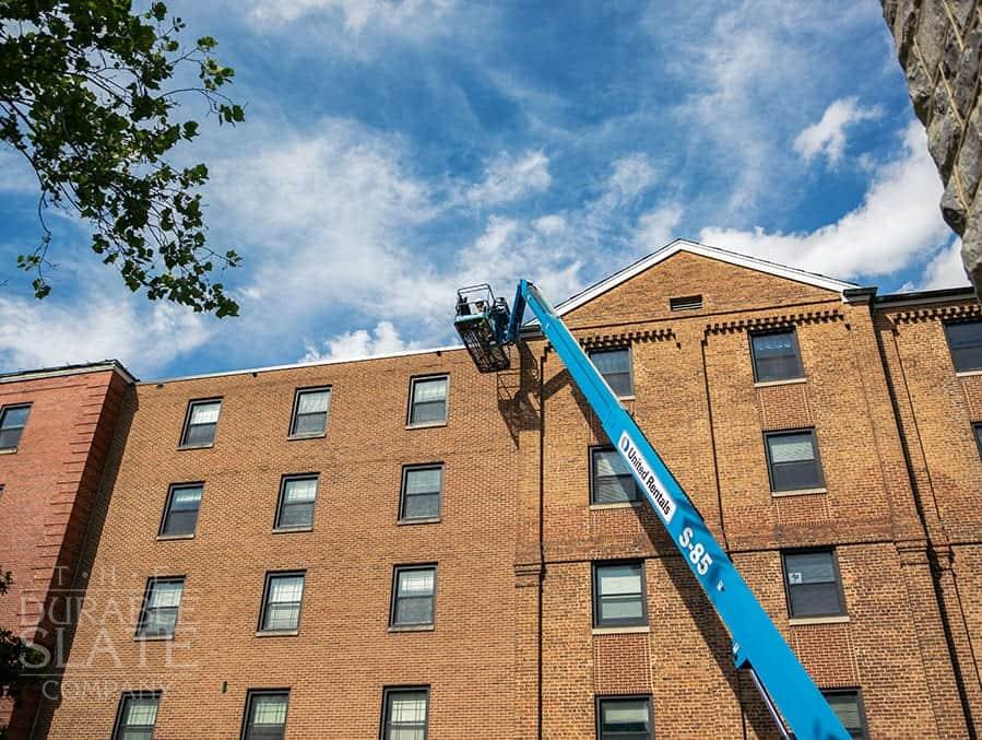 durable slate employee being lifted to the roof of virginia tech to repair the slate roof and install new copper flashing