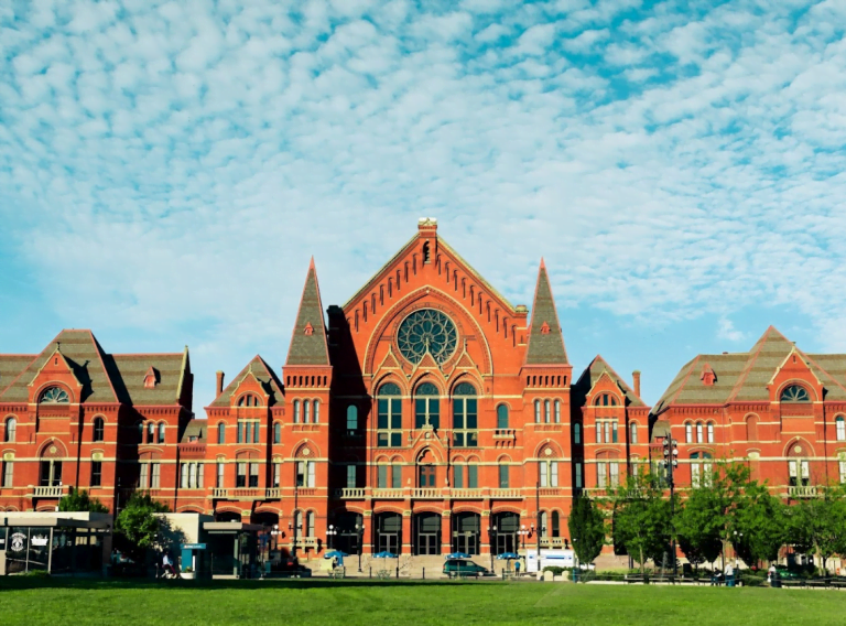 a large brick building with grass in front of a house with Cincinnati Music Hall in the background