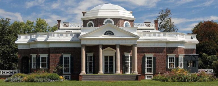 a large brick building with grass in front of a house with Monticello in the background