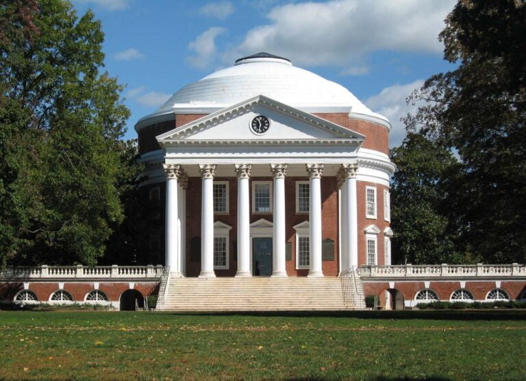 a large brick building with grass in front of a house with The Rotunda in the background